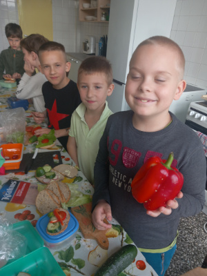 kuchnia uczniowie stół warzywa chleb chłopiec z papryką w dłoni